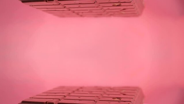 Close-up a milk ruby chocolate bar with chunks of nuts almonds and strawberry, displayed against a pink background is placed on a reflective surface, creating a mirrored image of itself