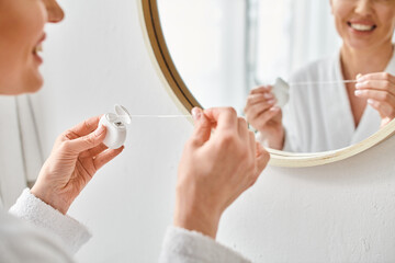 cropped view of adult woman in cozy bathrobe cleaning her teeth with dental floss in bathroom - obrazy, fototapety, plakaty