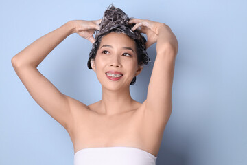 Young Asian woman applying shampoo on blue background, closeup