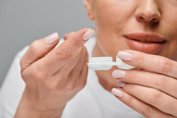 cropped view of concentrated female model wearing contact lenses carefully on gray background