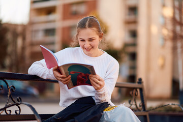 A beautiful blonde teenager sits on a bench in the park, taking a break from school to immerse...
