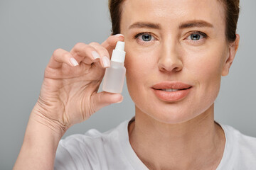cheerful good looking woman holding eye drops and looking straight at camera on gray backdrop