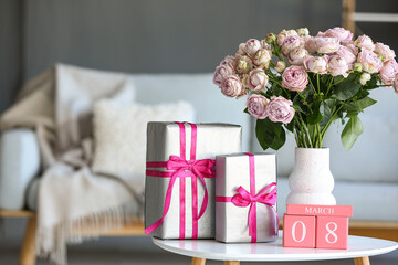 Calendar with date of International Women's Day, roses and gift boxes on table in living room, closeup