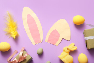 paper bunny ears with Easter eggs and gift boxes on lilac background