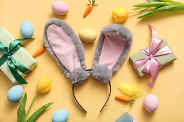 Bunny ears with Easter eggs, carrots and gift boxes on yellow background