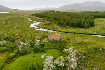 Beautiful aerial view of old rusty tin roof cottage, located in Connemara region in Ireland. Scenic Irish countryside landscape with mountains on the horizon, County Galway, Ireland.