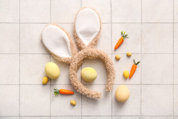 Fototapeta na wymiar Bunny ears with Easter eggs and carrots on white tiled background
