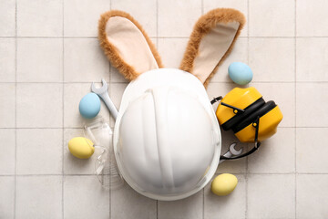 Bunny ears with Easter eggs, hardhat and construction worker tools on white tiled background