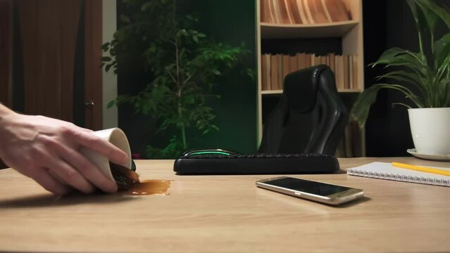 A clumsy office worker unfolded a cup of coffee on the desktop, turned over a cup of coffee at the workplace in the office, slow motion