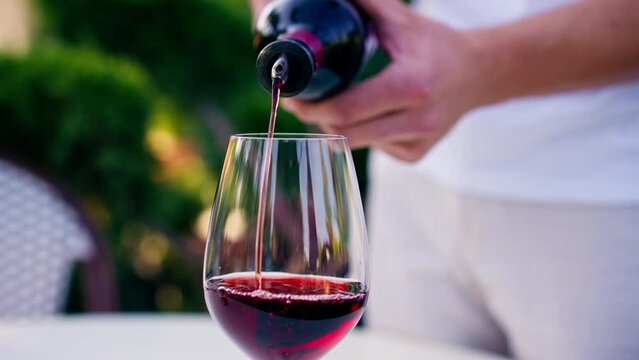 Close-up of a male sommelier's hand pouring aged wine from bottle into a glass for tasting on a vineyard