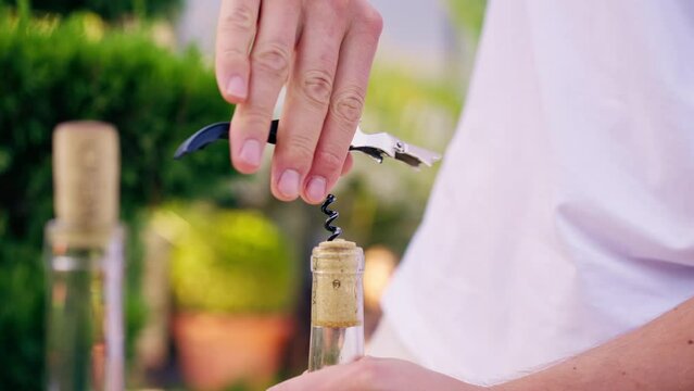 Close-up shot of a male sommelier's hand using a corkscrew to unscrew the wooden cork of wine bottle