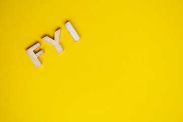 Top view of wooden FYI text on yellow background with customizable space for text