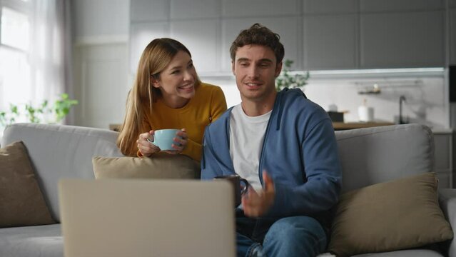 Happy lovers calling laptop drinking coffee at home. Family talking computer