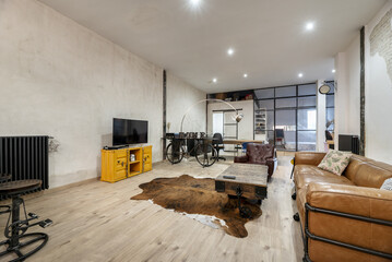 Large living room in a loft-style house with a brown leather sofa, synthetic leather on the floor,...