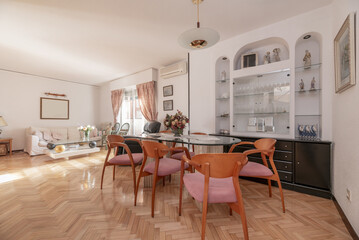 living room of a house with a three-seater light fabric sofa, a glass and marble coffee table and a glass dining table with marble feet and cherry wood chairs
