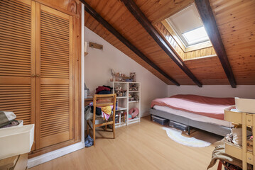 A wooden attic bedroom with a large integrated skylight, wooden desk and built-in wardrobe with...