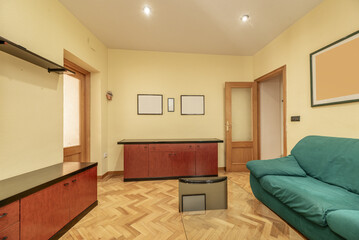 A living room with access to other rooms, French oak parquet floors, a modular bookcase with black edges, light yellow painted walls and a green microfiber sofa