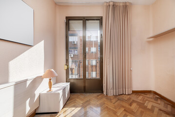 A small bedroom in a house with light wooden furniture, varnished oak parquet floors, a large window with curtains and access to a balcony