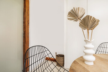 A circular wooden dining table with black metal railing chairs and a decorative vase