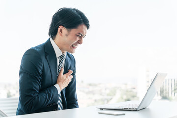 オフィスで胸を抑える若いアジア人ビジネスマン（心筋梗塞・発作・苦しい・急病・心臓発作・ストレス）
