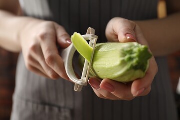 Woman peeling fresh zucchini indoors, closeup view