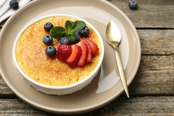 Delicious creme brulee with berries and mint in bowl on wooden table, closeup