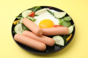 Delicious breakfast with boiled sausages and fried egg on yellow background