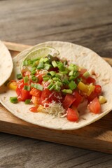Delicious taco with vegetables, green onion, lime and ketchup on wooden table, closeup