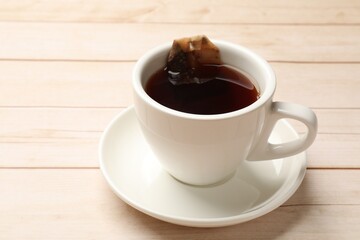 Tea bag and cup of hot beverage on light wooden table, closeup