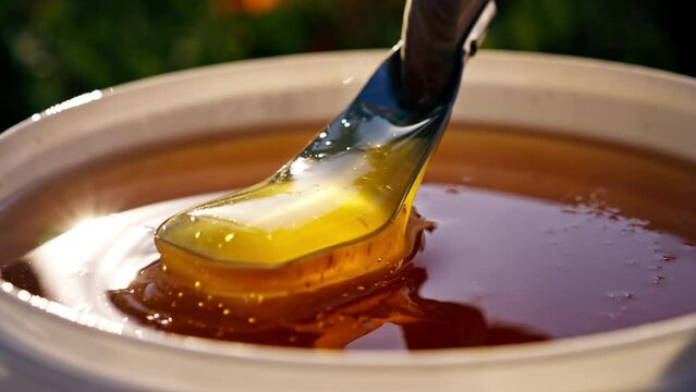 close-up hand with metal spoon mixing natural liquid honey flowing back into a large bowl at a mead or winery