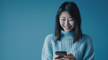 Smiling charming brunette Asian woman uses mobile phone happy texting in social networks addicted to modern technologies wears casual jumper isolated over blue background Online commun : Generative AI - obrazy, fototapety, plakaty