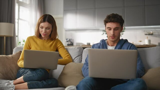 Involved pair working computers at couch closeup. Couple solving tasks together