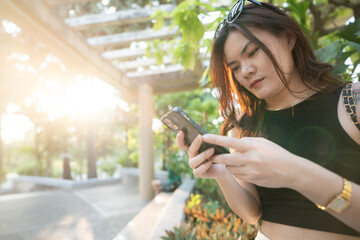 Business casual asian woman use smartphone in city park sunset light