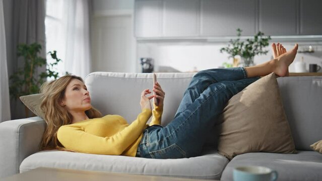 Relaxed woman browsing smartphone chilling couch at home. Lady creating message