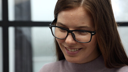 The face of a woman with glasses is a close-up in the office, she is working on a laptop