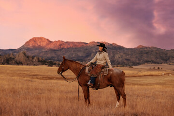 Cowgirl on roan quarter horse in the mountains at sunrise alpenglow