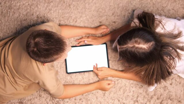 Mother and child lying on rug, learning with tablet. Child explores digital world as mother guides. Witness learning and family engagement engagement as they learn together, bonding over technology