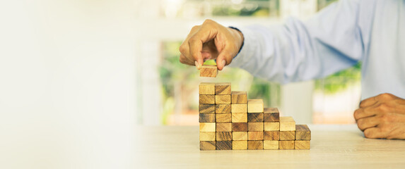 Hand placing wooden block tower stack in pyramid stair step with caution to prevent collapse or...