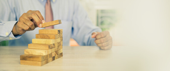 Hand placing wooden block tower stack in pyramid stair step with caution to prevent collapse or...