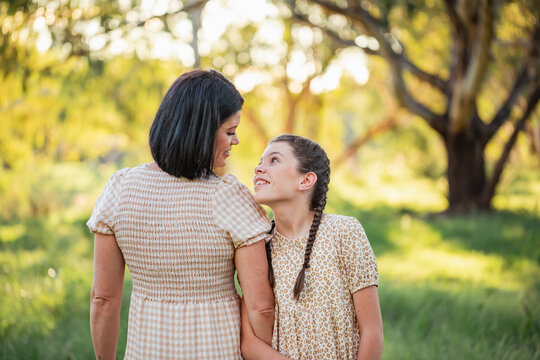 Pre-teen girl leaning on mother's shoulder in natural bush setting