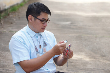 Asian man hold small magnifying glass to inspect detail and pattern of amulet. Concept, faith and...