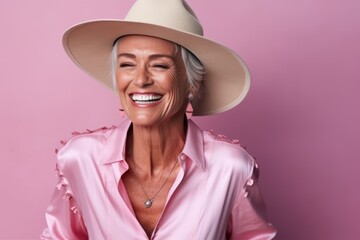 Portrait of happy senior woman in pink blouse and hat over pink background