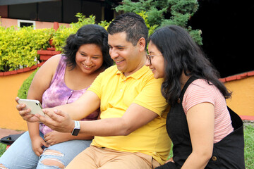 Divorced single dad with his dark-skinned Latino teenage daughters spending fun time using cell phone taking photos selfies