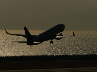 太陽光が反射する海面を背景に離陸していく飛行機