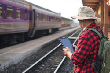 Asian man traveller is at railway station, holds smart tablet. Concept, travel by train in Thailand...