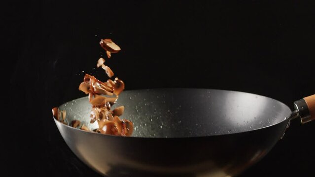 Chef cooking mushrooms on wok frying pan close up. Champignons mushroom with salt in pan. Restaurant Food concept