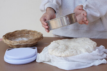 Closeup hand holds colander, dough flour for making bread or pizza, basket, scale on cookng table. Concept, cooking. Kitchen lifestyle. Preparing food. Bakery. Love cooking              