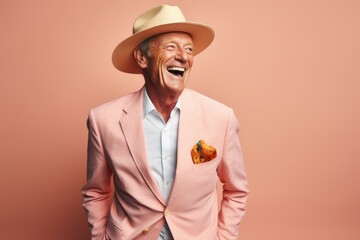 Elderly man in a hat and a suit on a pink background.