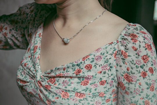 The chest of a woman wearing a floral dress and a silver pendant around her neck.