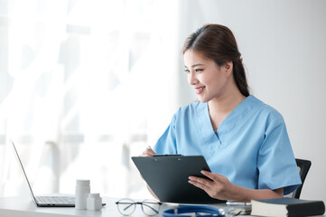 Asian female doctor working on laptop, filling out paperwork, patient medical history, reviewing documents at her workplace medical and health concept